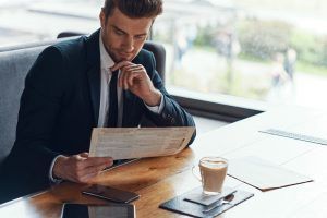 Handsome young businessman in full suit reading menu while sitting in the restaurant